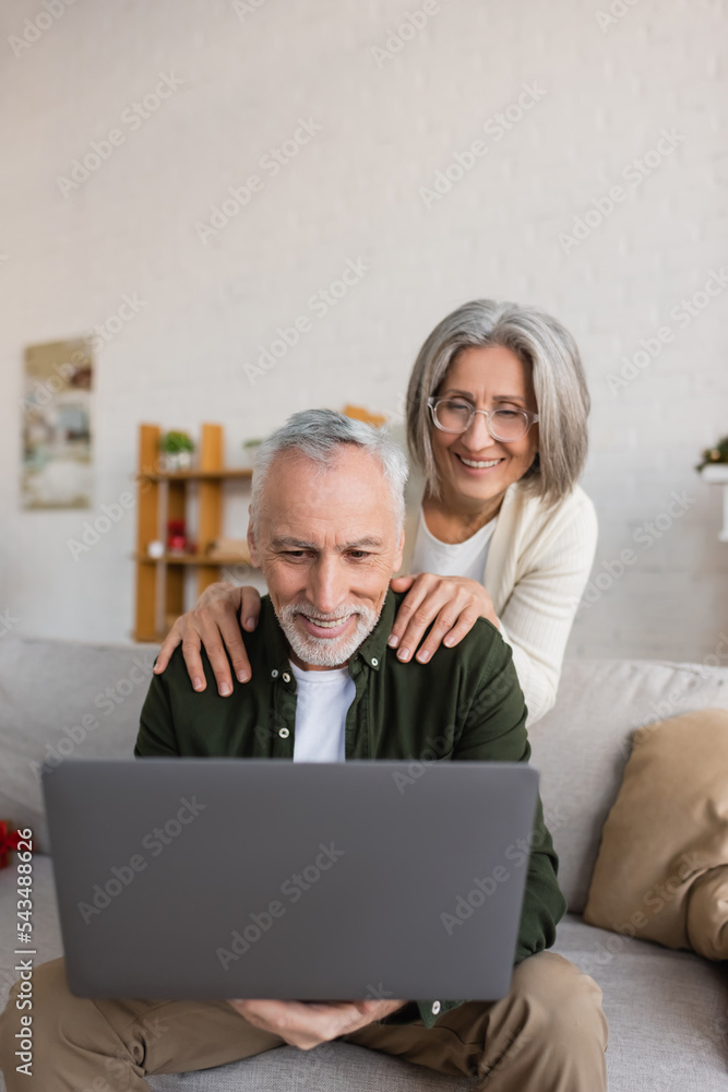 cheerful middle aged woman in glasses hugging husband during video call on laptop
