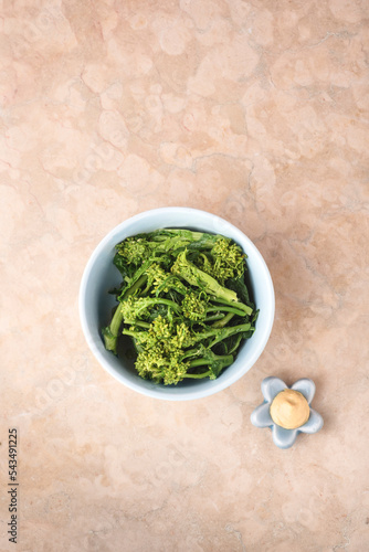 Broccolini Karashi-Ae (Hot mustard dressing) or turnip greens Nanohana seasoned with strong mustard called Karashi together with soy sauce, pink marble background. Spring Japonese dish, top view