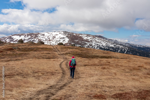 Woman with backpack hiking in cold windy winter at Ladinger Spitz in the Saualpe mountain range, Lavantal Alps, Carinthia, Austria, Europe. Hike path along on alpine pasture, clouds. Tourism Wolfsberg photo