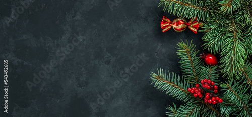 Christmas dark grunge horizontal background, top view. Fir twigs, red golden berries, baubles. Winter holidays, New Year decoration, pine tree branches, snow covered cones, flat lay, copy space.