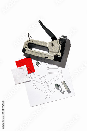 Silver furniture stapler gun with staples and the drawing of the armchair isolated on white background. Manual industrial tool