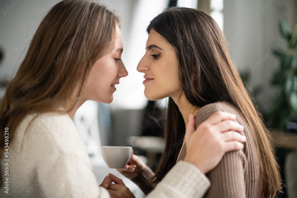 Side view of woman in sweater hugging partner with cup at home Side view of woman in sweater hugging partner with cup at home