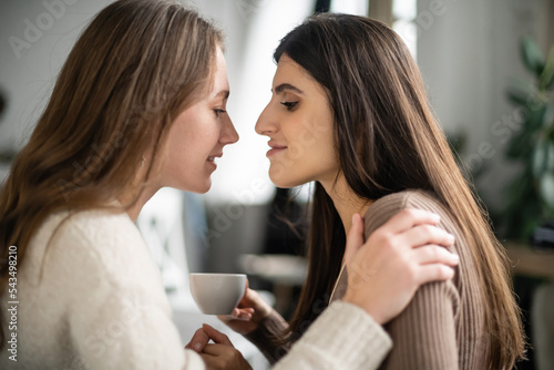 Side view of woman in sweater hugging partner with cup at home