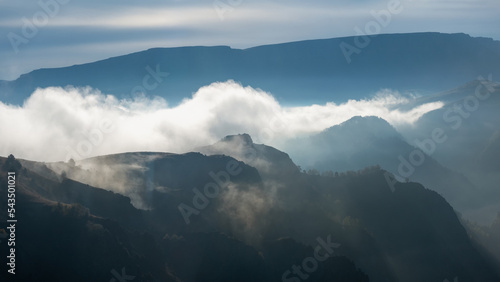 Wonderful scenery with great Caucasus rocks and mountains in dense low clouds. Atmospheric highlands landscape with mountain tops under clouds. Beautiful panoramic view to forest mountain peaks.