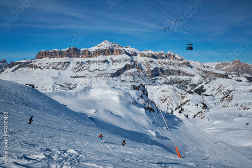 View of a ski resort piste with people skiing in Dolomites in Italy with cable car ski lift. Ski area Arabba. Arabba, Italy