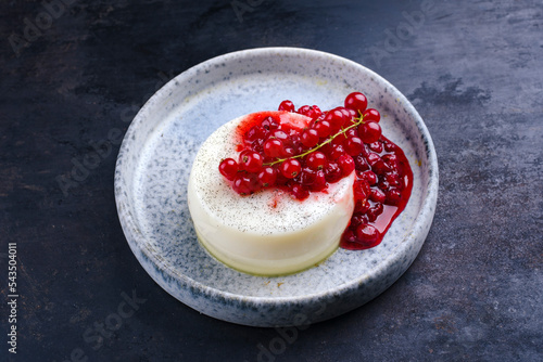 Traditional vanilla pudding fresh currants and compote served as close-up in a Nordic design plate on a black board