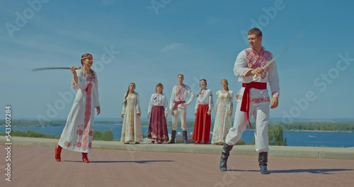 Beautiful martial art of flanking with sabers. Man and a woman in beautiful national costumes with embroidery flank with sabers, the Slavs look at them. 4k, ProRes photo