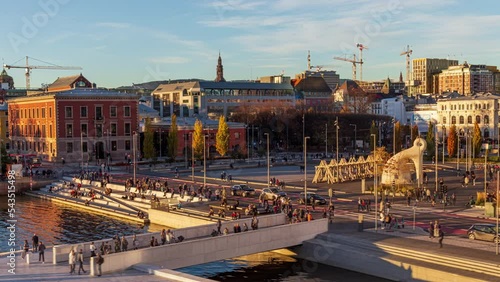 Oslo Norway hyper-lapse: sunny afternoon cityscape and skyline of city center square. Time-lapse of people walking hurriedly across the bridge over water canal and casting long shadows.