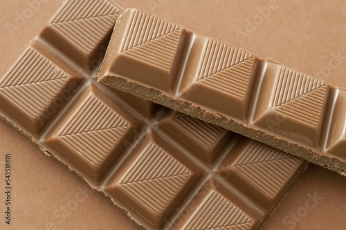 High angle shot of stacked broken bars of milk chocolate against brown background