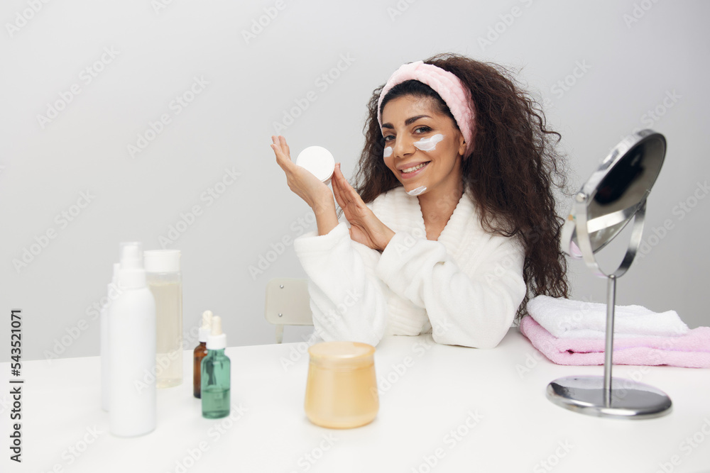 Enjoying beauty procedures cheerful smiling tanned pretty curly Latin lady present favorite facial cream in home interior. Copy space. Aesthetic medicine skincare cosmetic brands ad concept