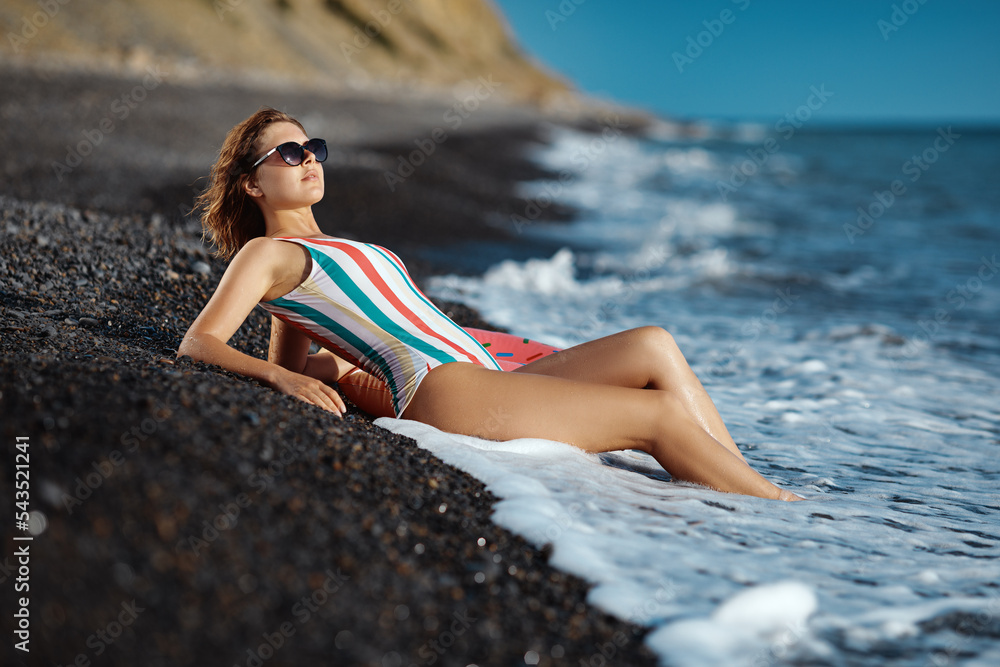 Tanned young woman in a swimsuit and sunglasses enjoying the water.