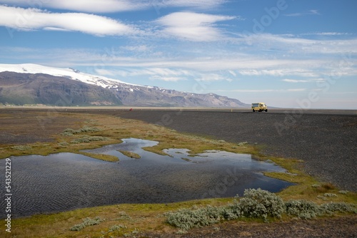 Waterscape surrounded by grass in Iceland with a highway and glacier mountains in the background