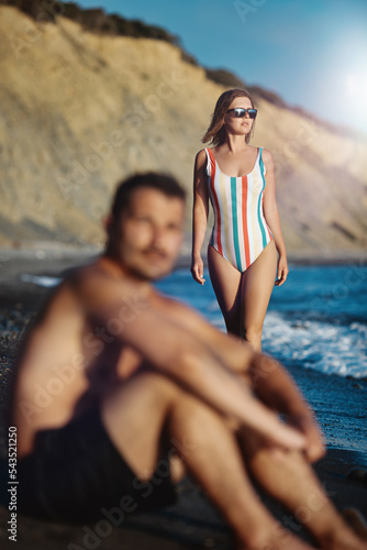 Obraz na płótnie Young couple on the beach. Focus on the woman looking at the see in the background. Shallow depth of field. w salonie