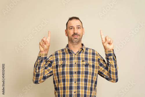 Portrait of a happy bearded man pointing fingers at copyspace isolated over beige background.