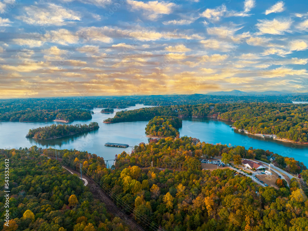 Lake Lanier in North Georgia, 4K aerial drone on a sunny fall day. Radiant clouds both blue and orange. Clear view of fall colored trees and blue lake water.