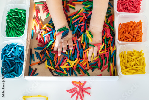 Child hands playing with dyed pasta for sensory play and craft activities. Learning colors activity for kids, activities Montessori, games for fine motor skills, play for toddler.