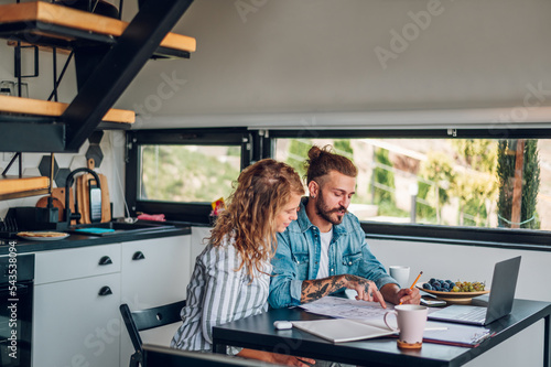 Fotografie Happy couple using laptop and looking into blueprints of their new home