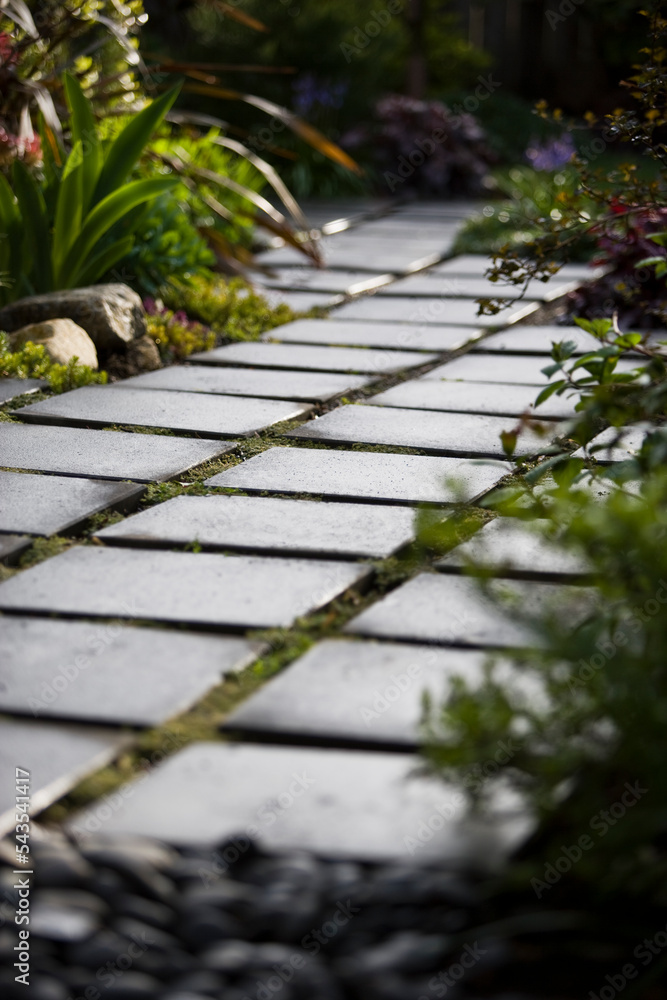 A modern walkway of black tile pavers provides sharp contrast to the green landscape of a garden patio