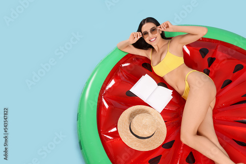 Young woman with book on inflatable mattress against light blue background