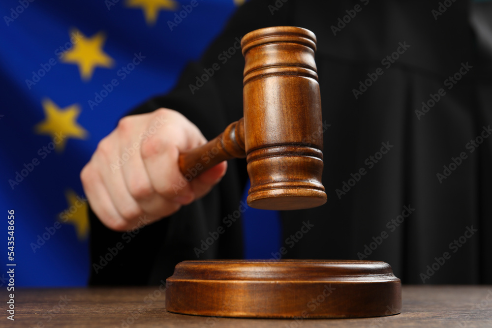 Judge with gavel at wooden table against flag of European Union, closeup Judge with gavel at wooden table against flag of European Union, closeup