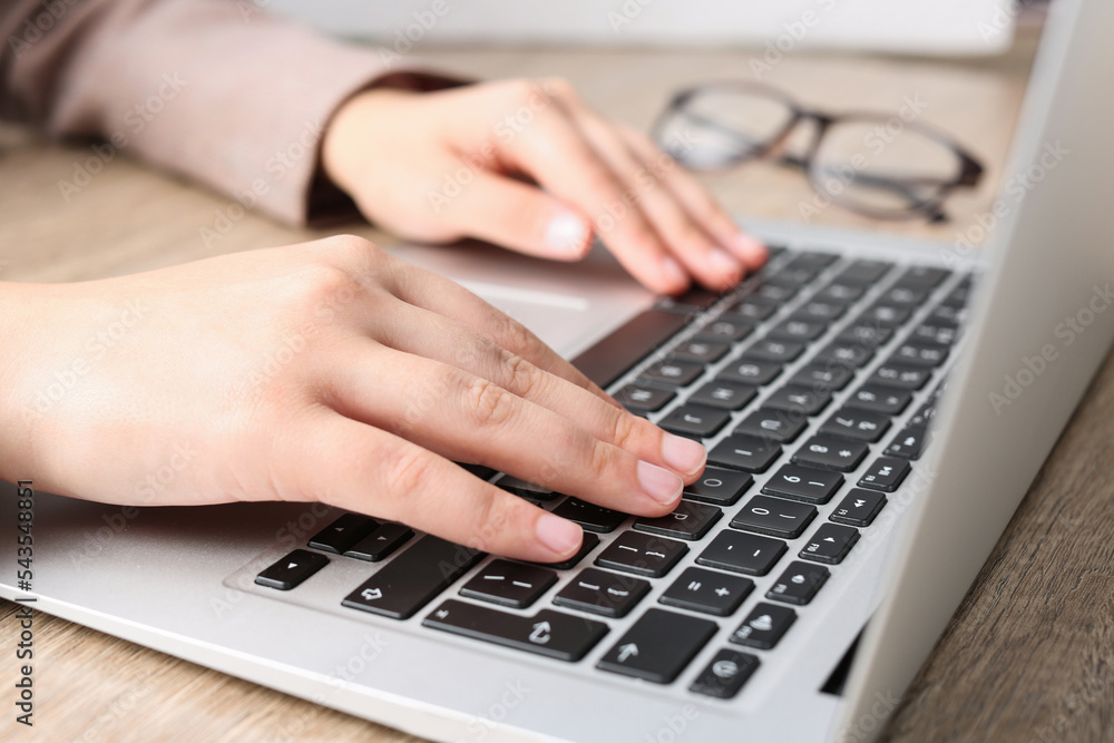 Woman working on laptop at wooden table, closeup Woman working on laptop at wooden table, closeup