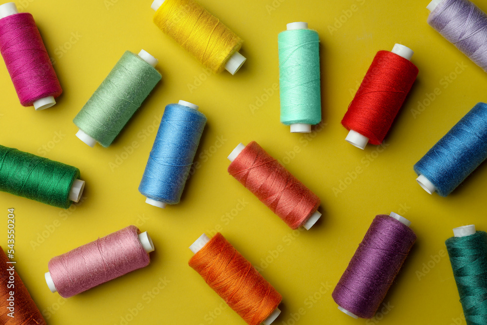 Different colorful sewing threads on yellow background, flat lay Different colorful sewing threads on yellow background, flat lay