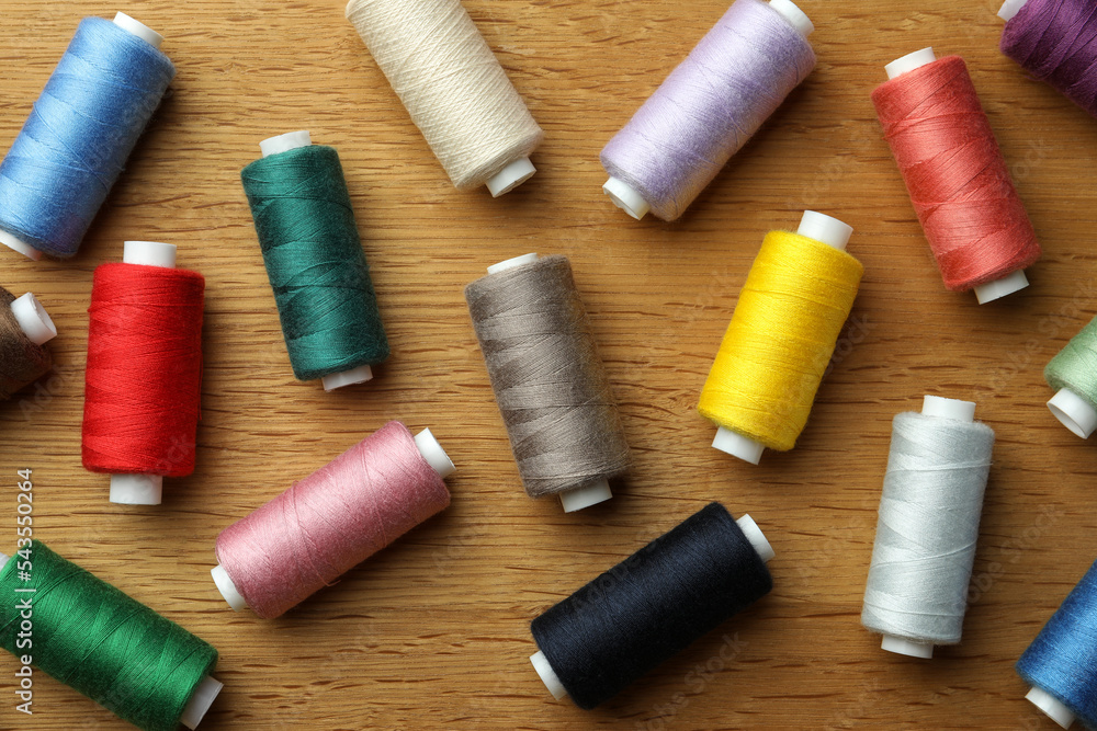 Many colorful sewing threads on wooden table, flat lay Many colorful sewing threads on wooden table, flat lay
