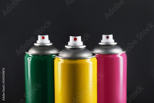 Colorful cans of spray paints on black background, closeup