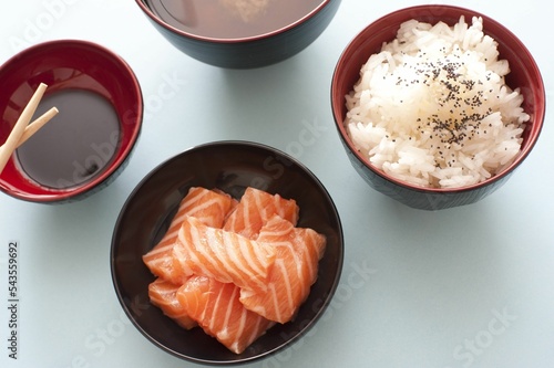 Overhead closeup of salmon chunks, steamed rice and soy sauce in dark bowls on a table