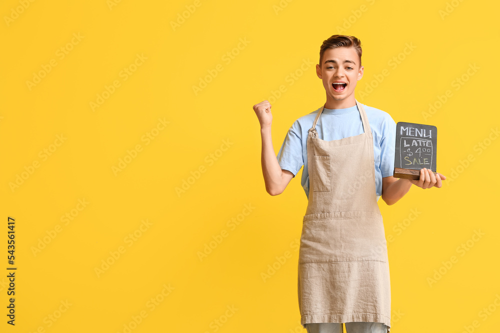 Happy male barista holding chalkboard with menu on yellow background Happy male barista holding chalkboard with menu on yellow background
