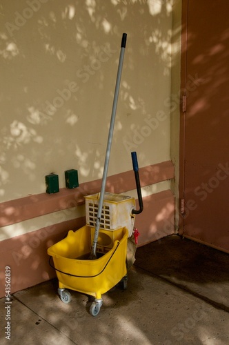 Yellow industrial mop bucket and mop outside wall in shade