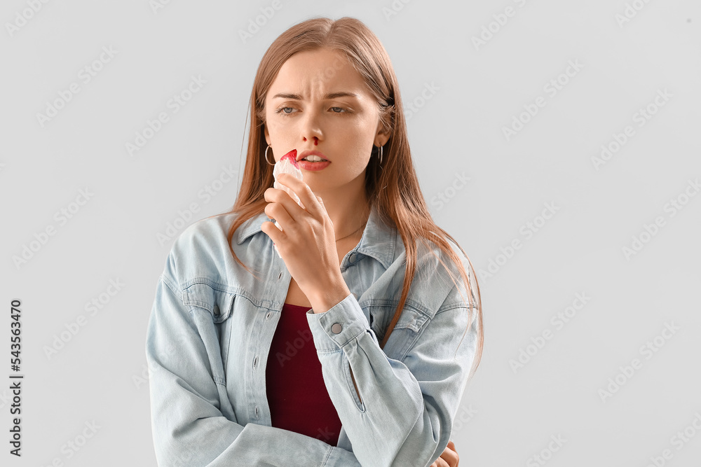 Young woman with nosebleed and tissue on light background Young woman with nosebleed and tissue on light background