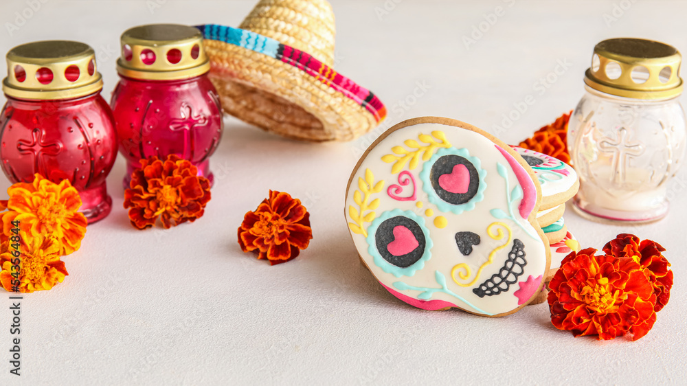 Skull shaped cookies, candles and flowers on white background. El Dia de Muertos