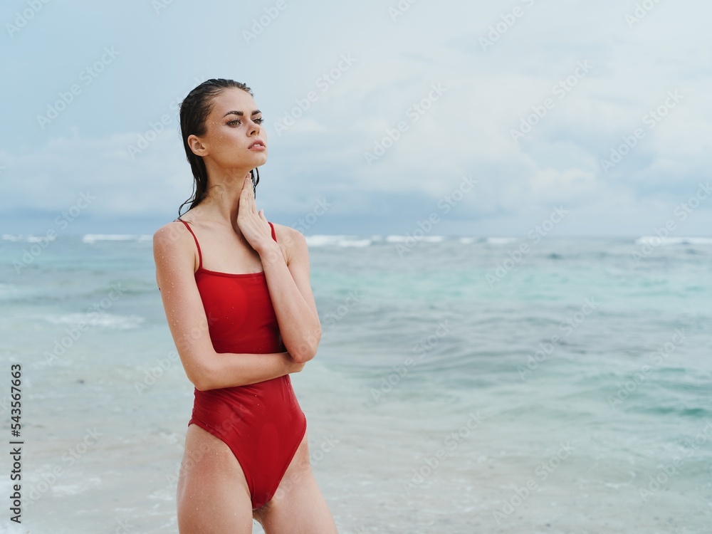 Beautiful sexy woman in a red swimsuit on the ocean beach with wet hair, slender pumped body sunscreen