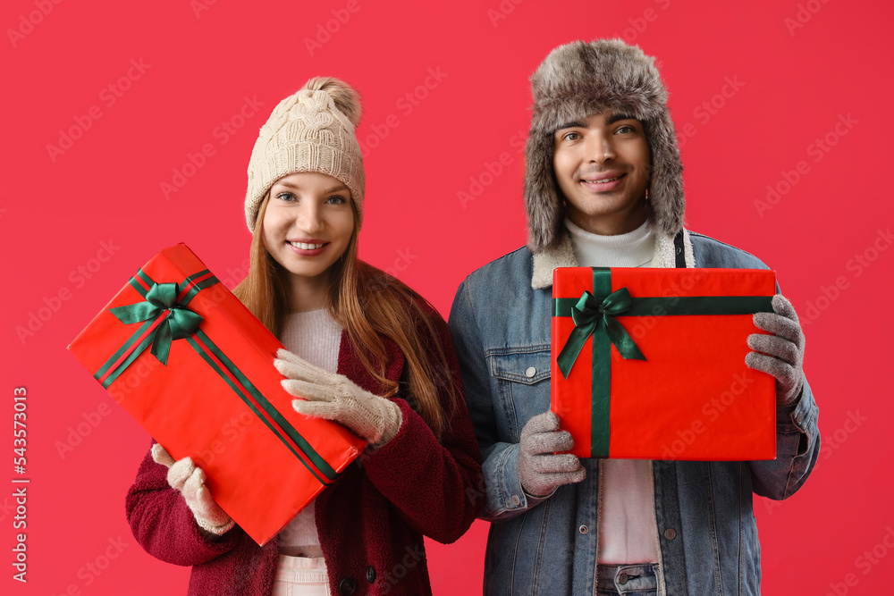 Happy young couple with Christmas presents on red background