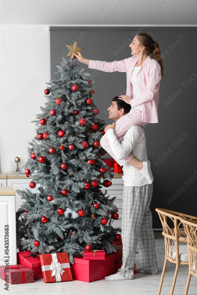 Loving couple decorating Christmas tree in kitchen Loving couple decorating Christmas tree in kitchen