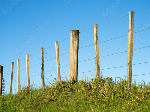 View of wire boundary farm fence with wooden posts