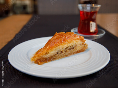 Piece of Carrot Slice Baklava (Turkish: Havuc Dilim Baklava) on white plate with glass of tea on table in cafe. Traditional Baklava from Gaziantep, Turkey. Baklava with walnut close up. photo