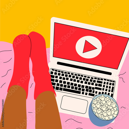 Woman lies on the bed and watches series on laptop with popcorn in her cute room.