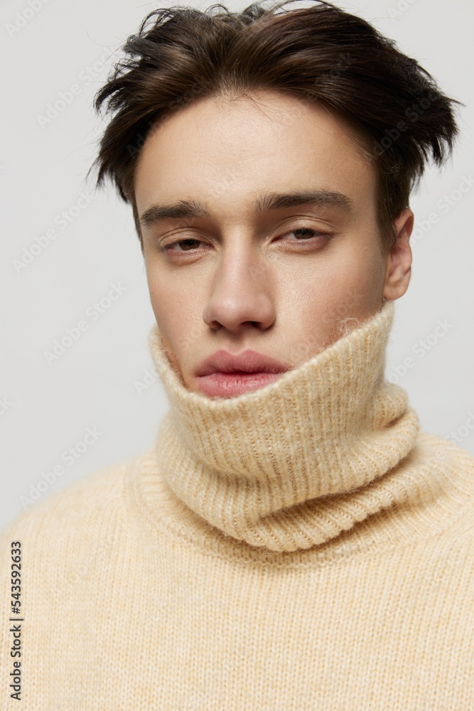 Portrait photo. vertical studio. close-up photo.Cute young man with dark combed back short curly hair in a beige sweater with a high neck stands on a gray background vertical studio photo Portrait photo. vertical studio. close-up photo.Cute young man with dark combed back short curly hair in a beige sweater with a high neck stands on a gray background vertical studio photo
