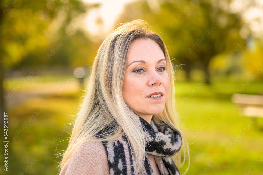 Portrait of a pensive middle-aged woman wearing a sweater and scarf in a park in autumn Portrait of a pensive middle-aged woman wearing a sweater and scarf in a park in autumn