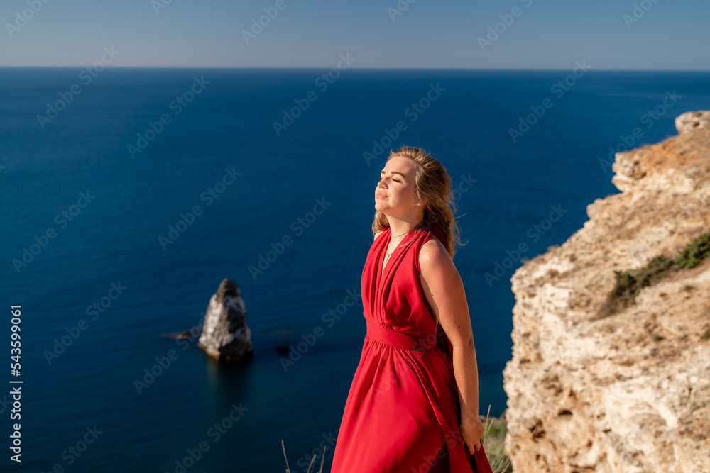 A woman in a red flying dress fluttering in the wind, against the backdrop of the sea. A woman in a red flying dress fluttering in the wind, against the backdrop of the sea.
