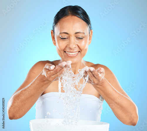Water splash, skincare and with a woman washing her face for beauty, self care and facial care on blue background for cosmetics or dermatology mockup. Health, wellness and natural model cleaning skin