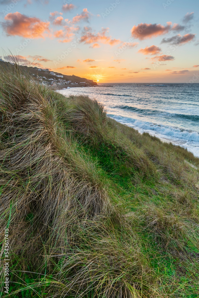 Stunning landscape image of Sennen Cove in Cornwall during sunset viewed from grassy sand dunes with dramatic sky and long exposure sea motion Stunning landscape image of Sennen Cove in Cornwall during sunset viewed from grassy sand dunes with dramatic sky and long exposure sea motion