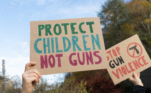 Protesters holding signs with slogans Protect Children Not Guns and Stop Gun Violence. People with placards at protest rally demonstration strike to ban weapons and end shooting.