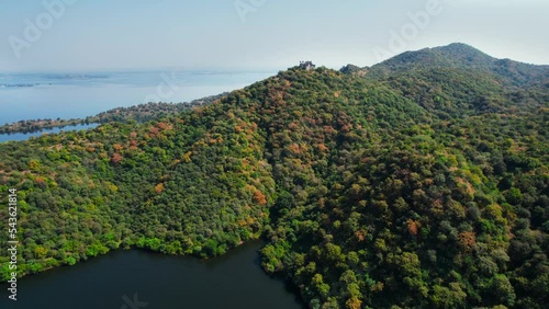 flying towards aerial drone shot of Ruthi Rani mahal at jaisamand surrounded by tree covered green aravalli hills and the blue waters of Dhebar lake. photo