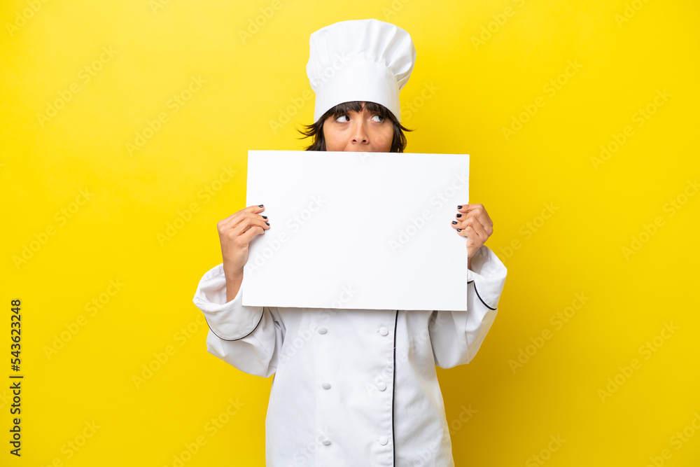 Young chef latin woman isolated on yellow background holding an empty placard and hiding behind it Young chef latin woman isolated on yellow background holding an empty placard and hiding behind it