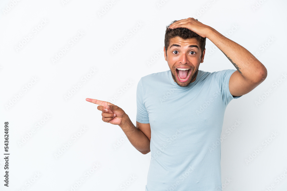 Young handsome Brazilian man isolated on white background surprised and pointing finger to the side Young handsome Brazilian man isolated on white background surprised and pointing finger to the side
