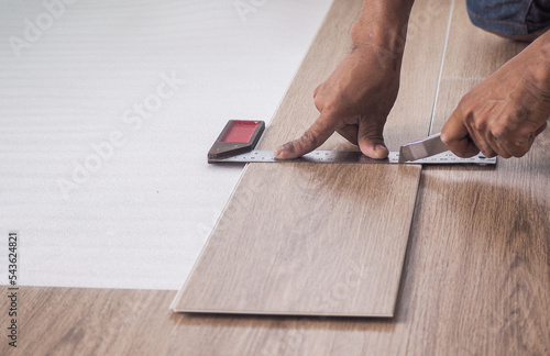 A technician is cutting luxury vinyl floor tiles with a cutter to lay the floor before placing it on the leveling foam. photo