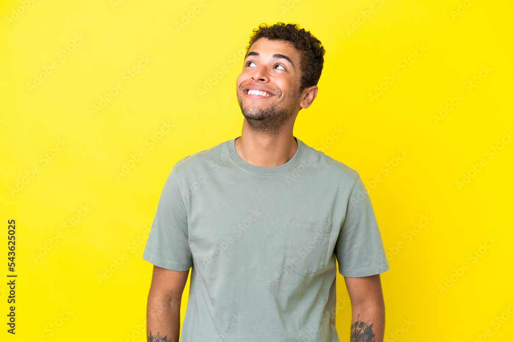 Young handsome Brazilian man isolated on yellow background thinking an idea while looking up Young handsome Brazilian man isolated on yellow background thinking an idea while looking up